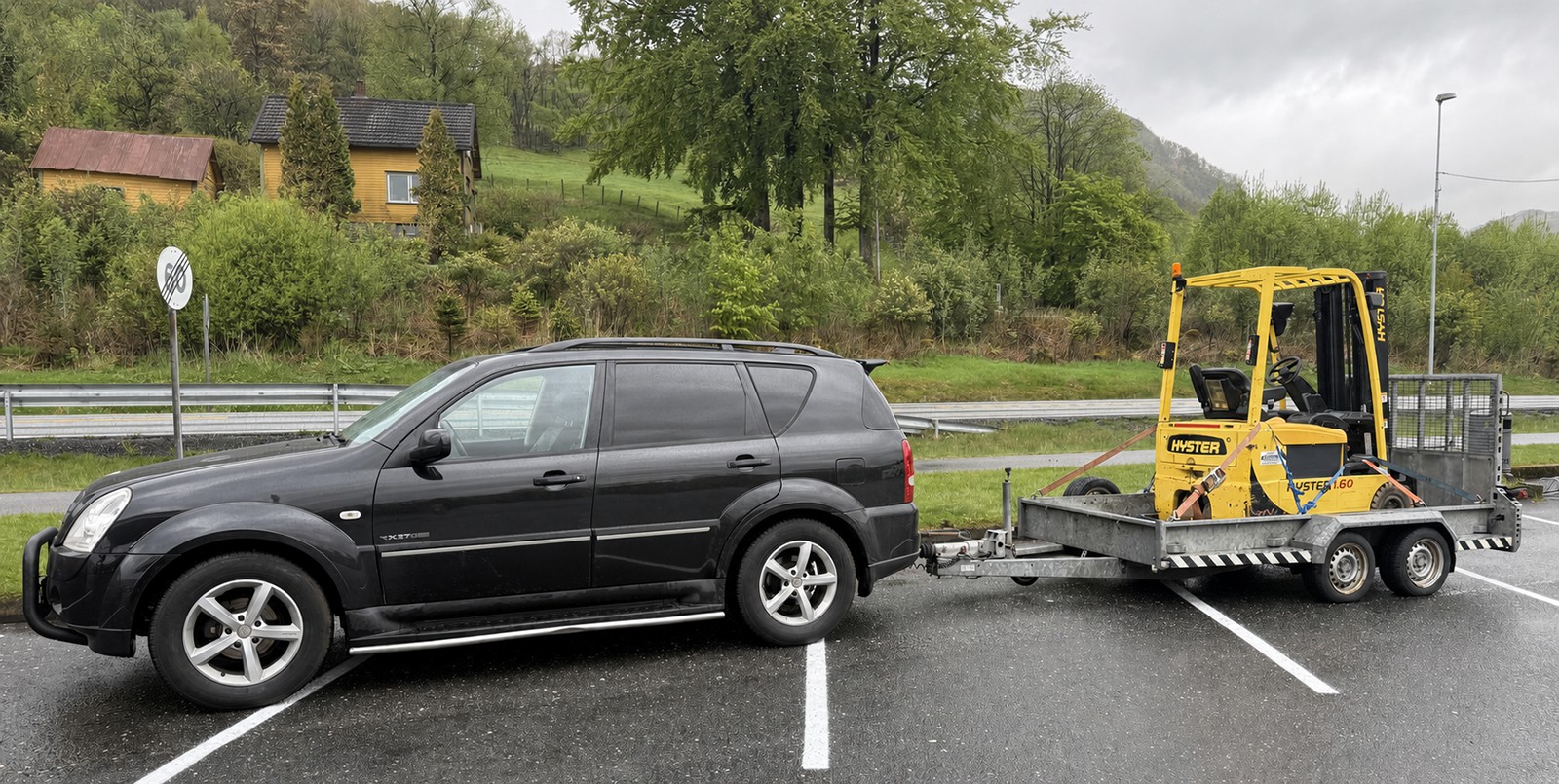 Svart SUV og gul Hyster-truck sikret på maskinhenger sett fra siden